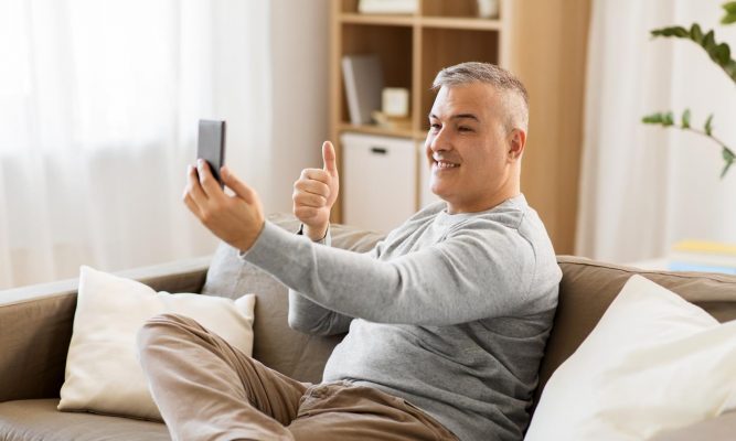 Man on a sofa making a video call and holding up his thumb