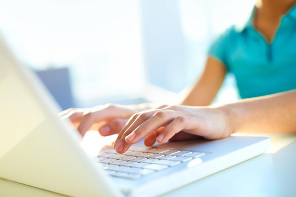 Woman in a turquoise top using a laptop keyboard