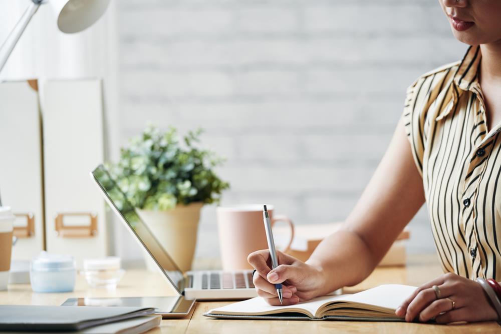 Woman using a laptop and making notes with pen and paper